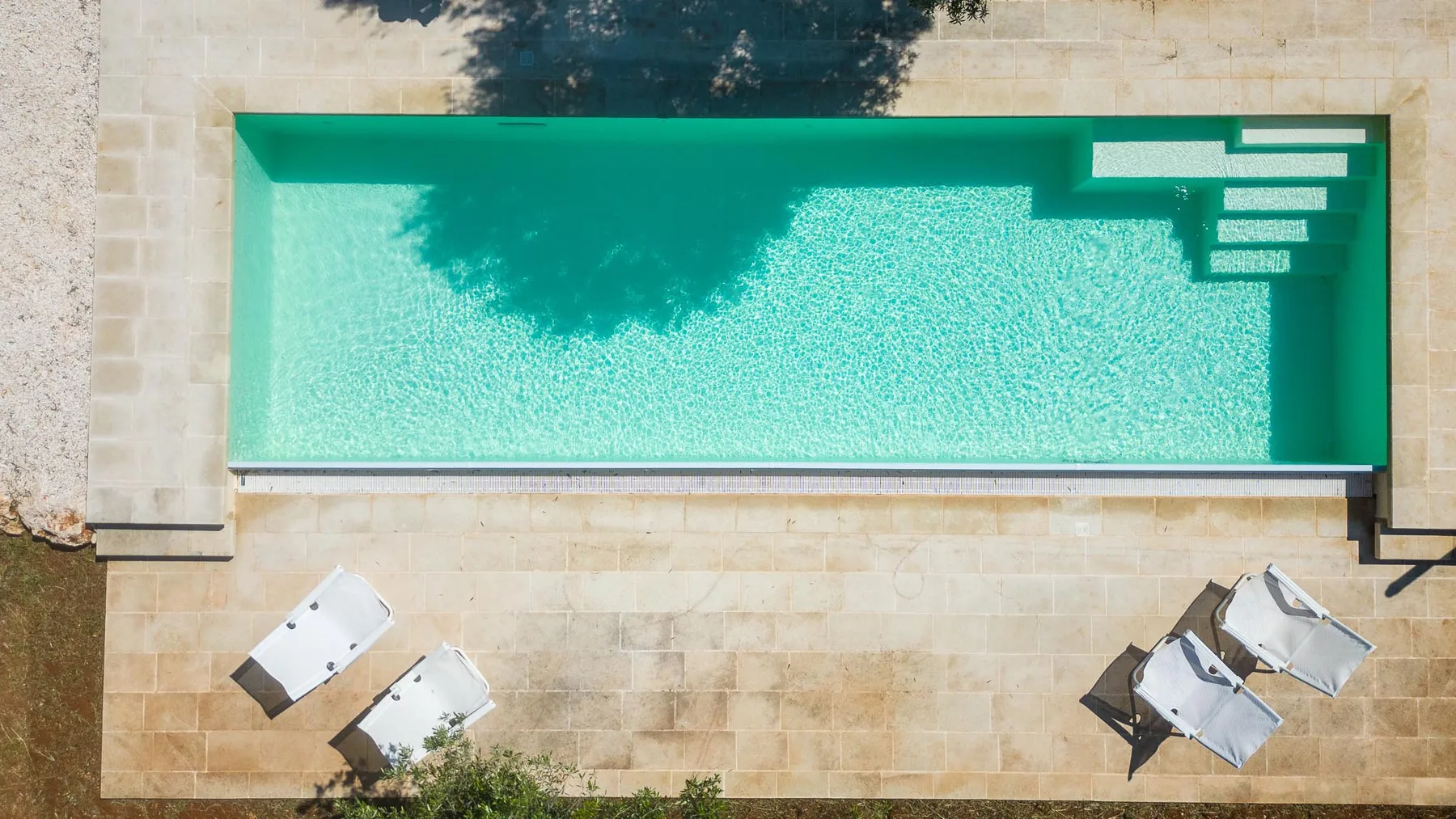 A rectangular swimming pool with pale stone paving and steps at one end.