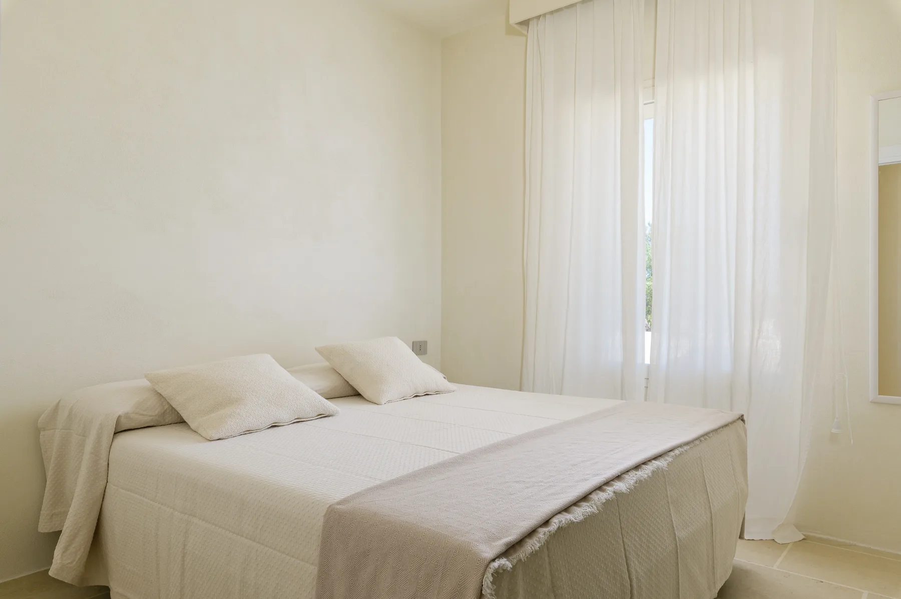 A bright bedroom with a bed and sheer curtains over the window.