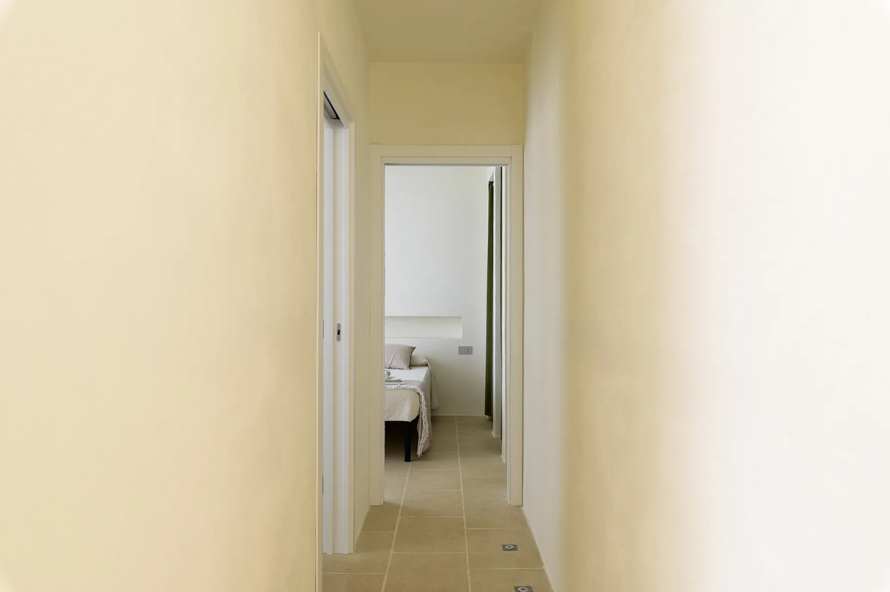 A narrow hallway leads to a bedroom with a bed visible through the doorway.