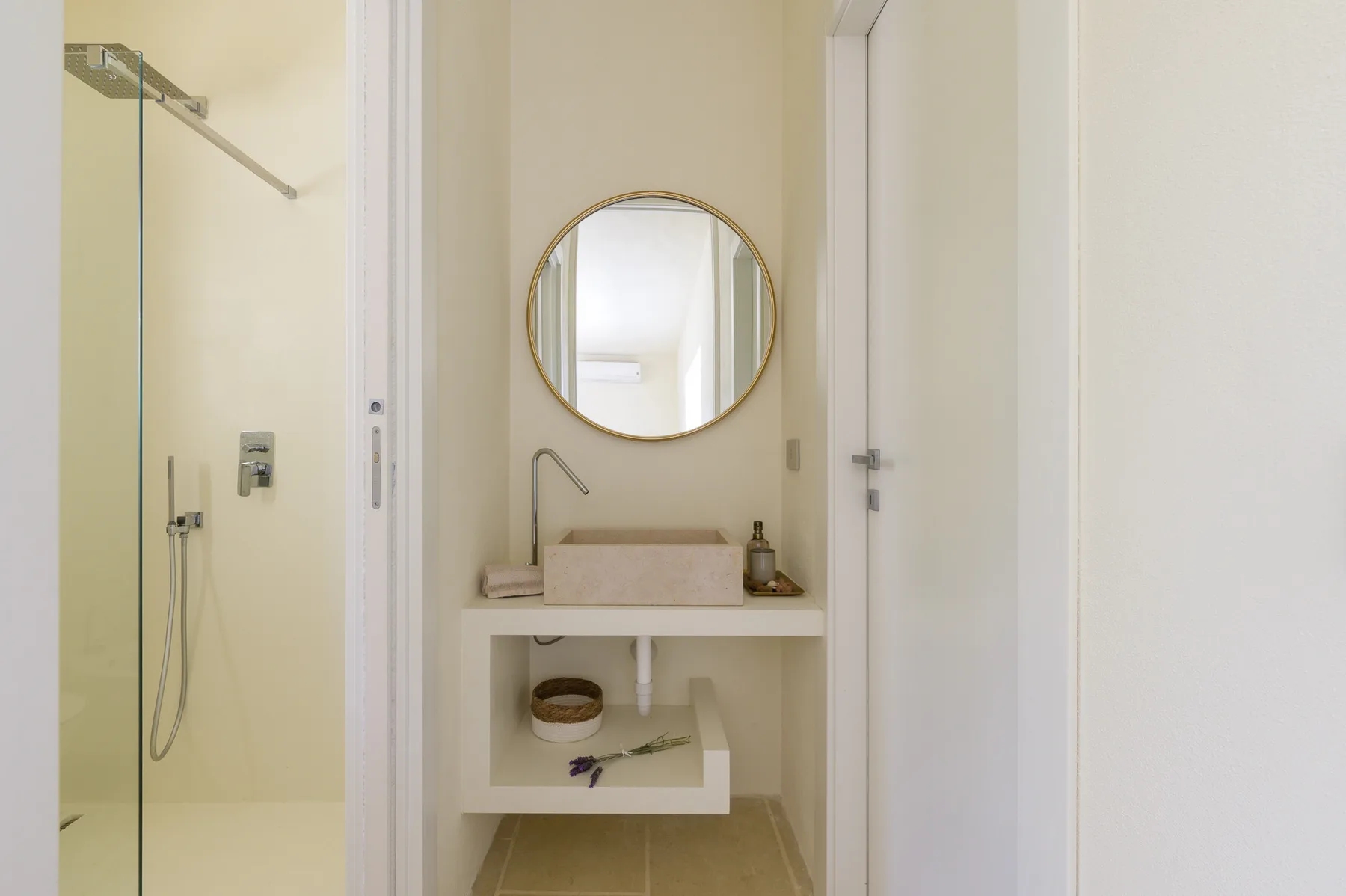 A bright bathroom with a glass shower and a small vanity beneath a round mirror.