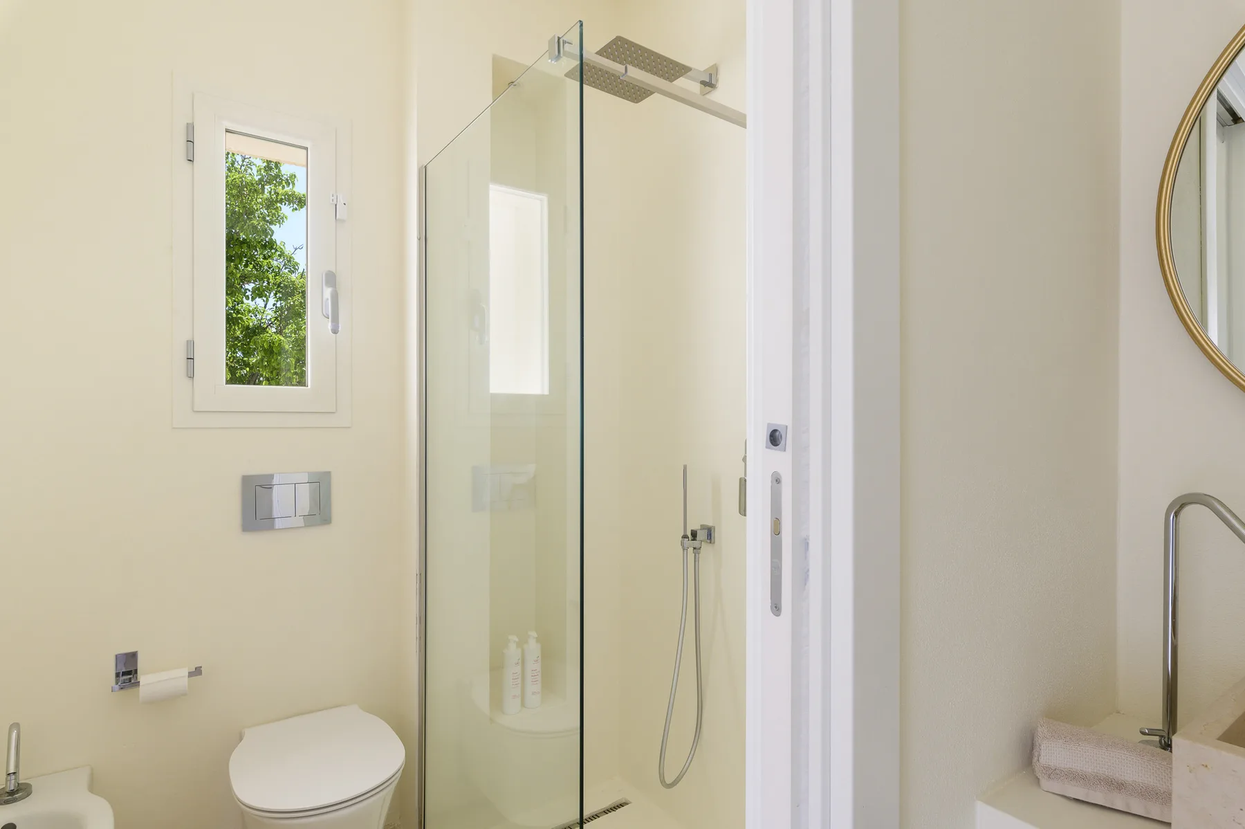 A bright bathroom with a glass shower and a window.