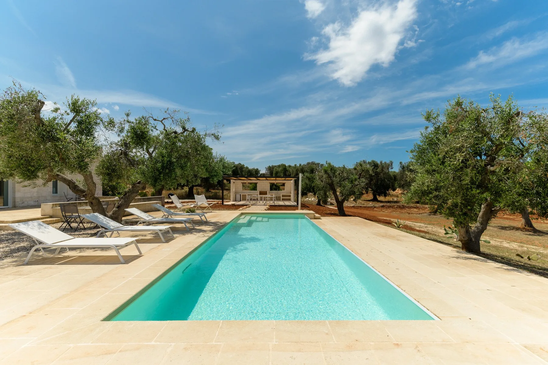 An outdoor swimming pool is surrounded by a paved deck and trees.