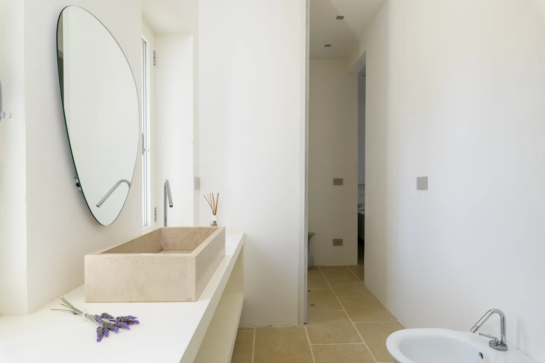 A bright bathroom vanity with a vessel sink, mirror, and a hallway beyond.