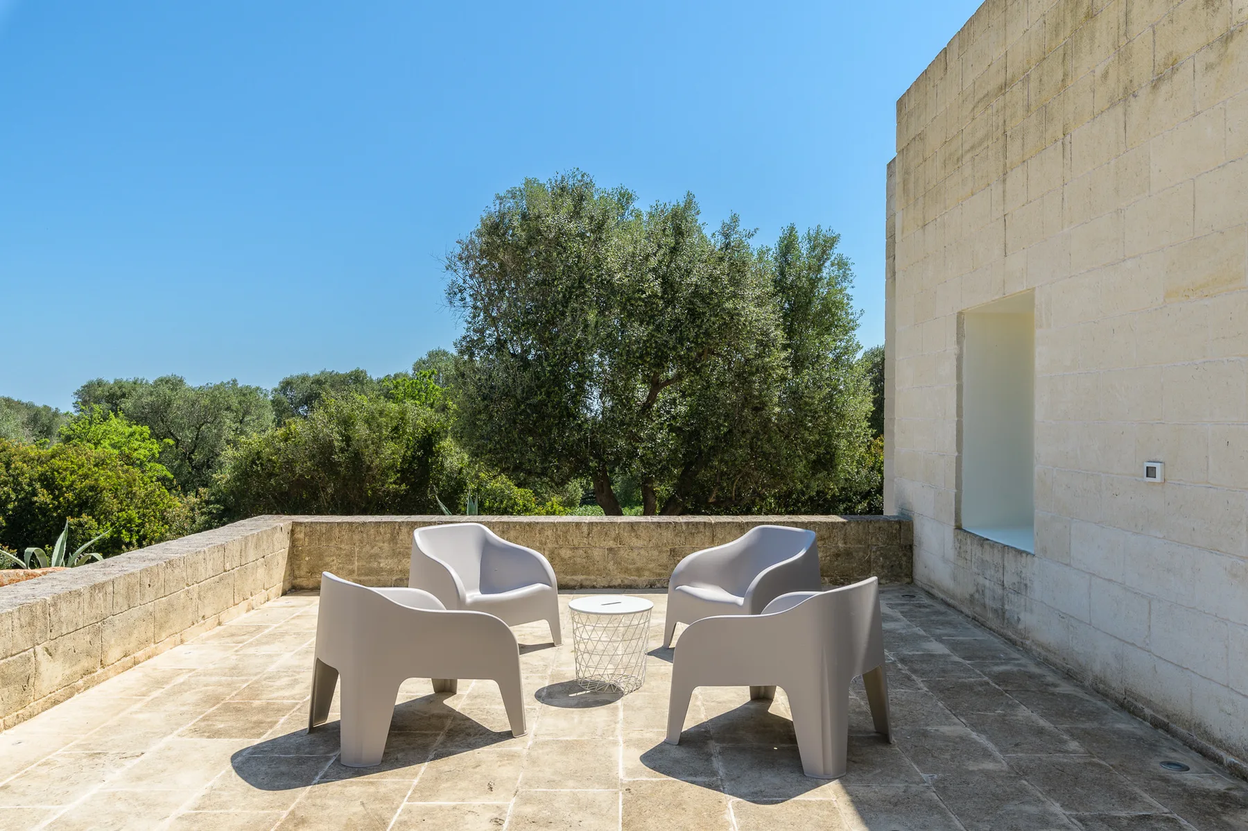 A sunny stone terrace has outdoor seating and views of surrounding trees.