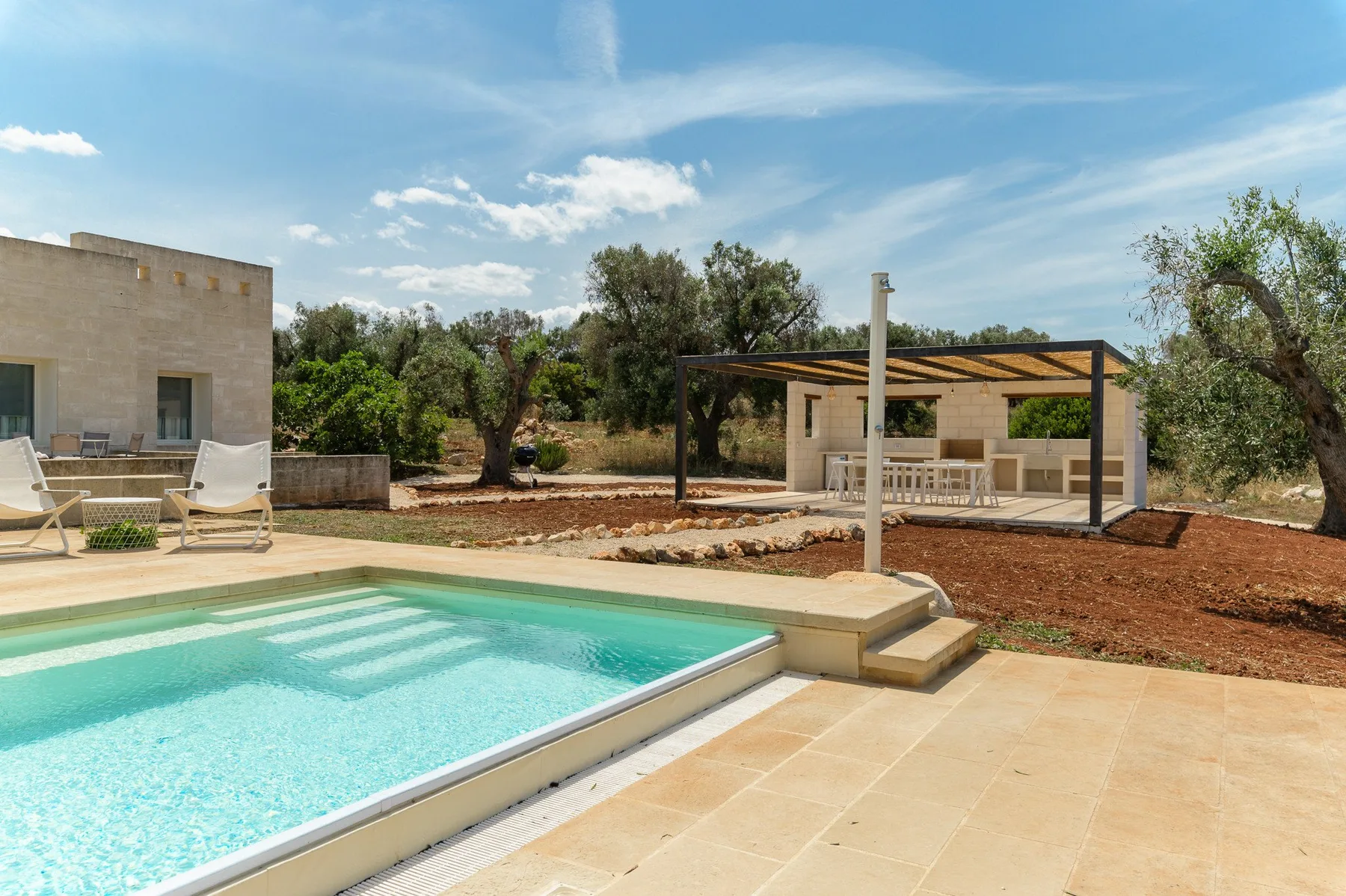 An outdoor swimming pool sits beside a shaded patio and landscaped grounds.