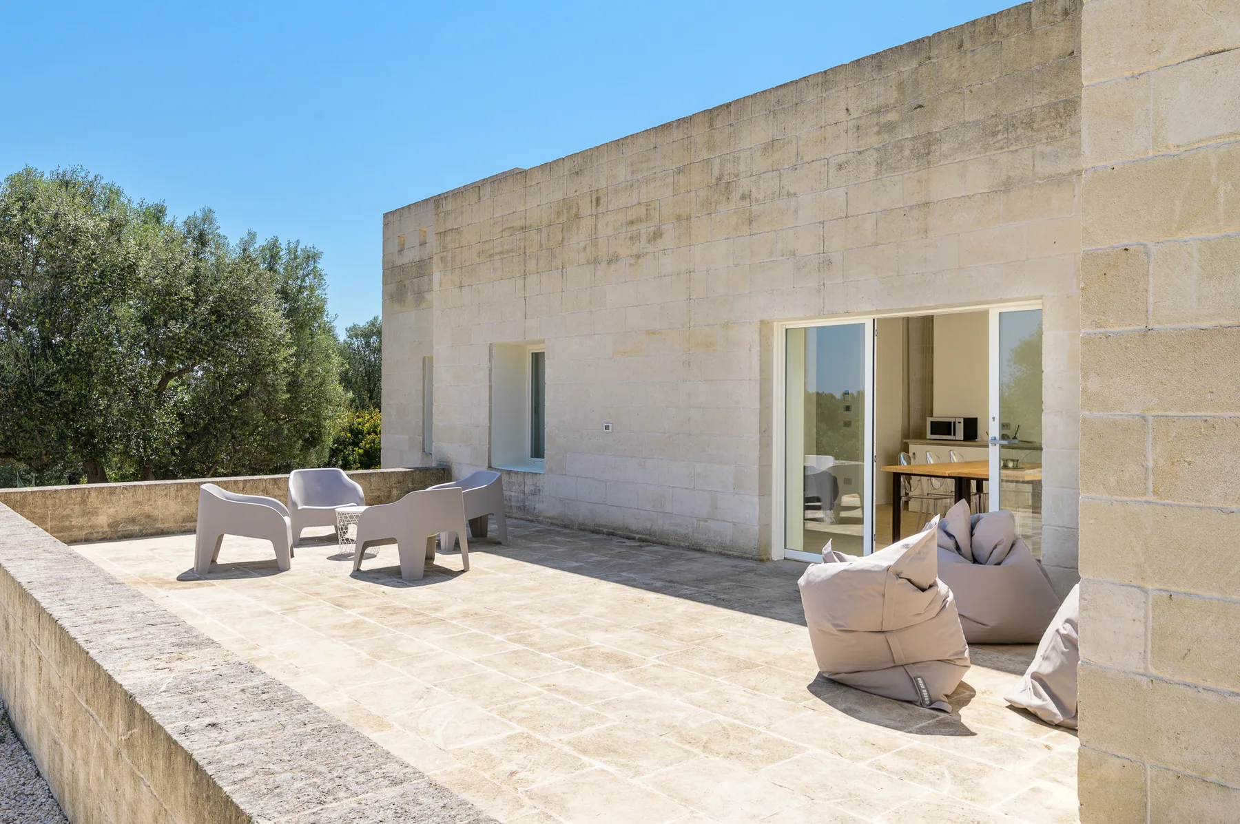 A sunlit stone terrace with outdoor seating beside an open glass doorway.