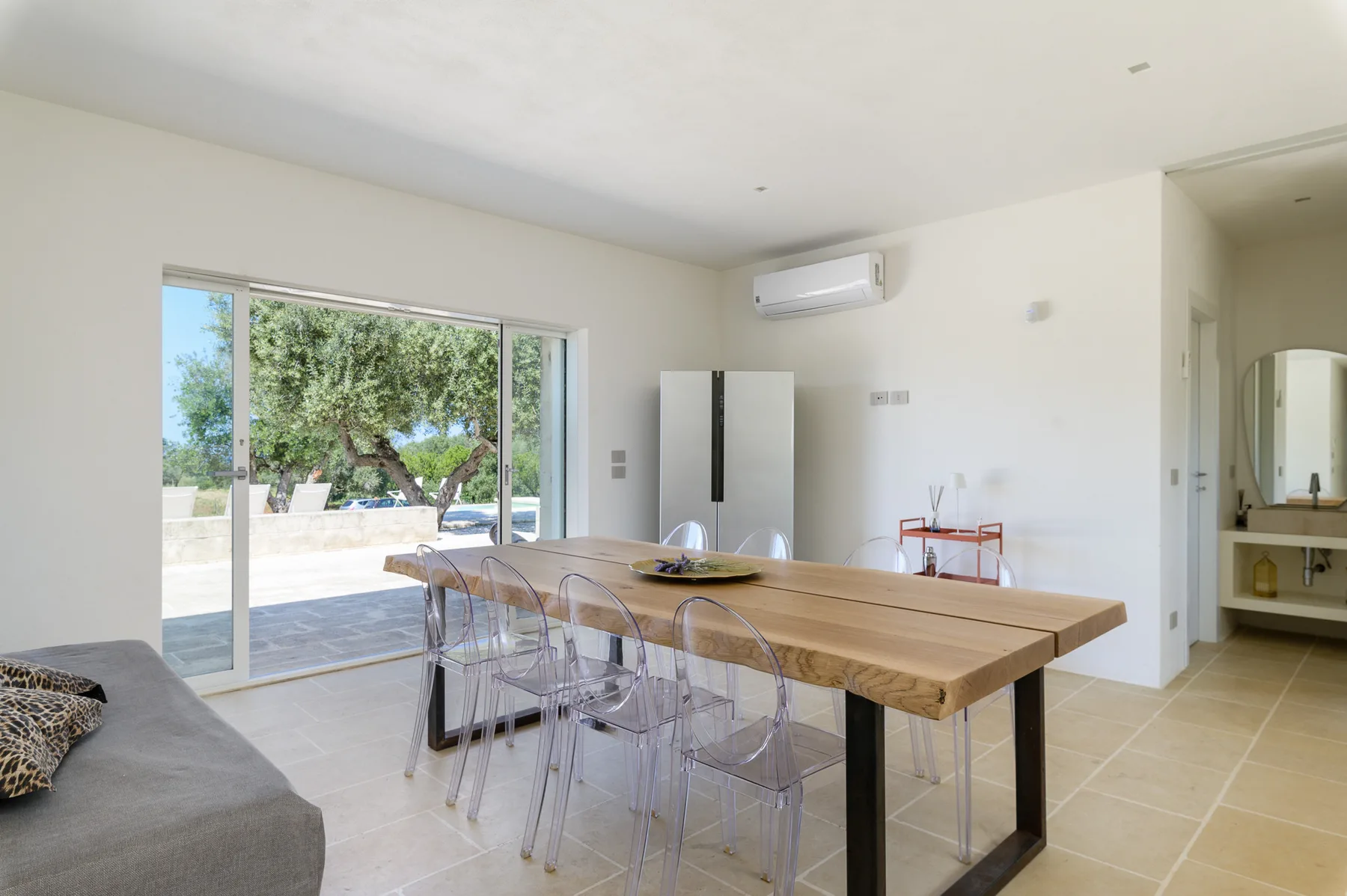 A bright dining area with a long wooden table beside large sliding glass doors.