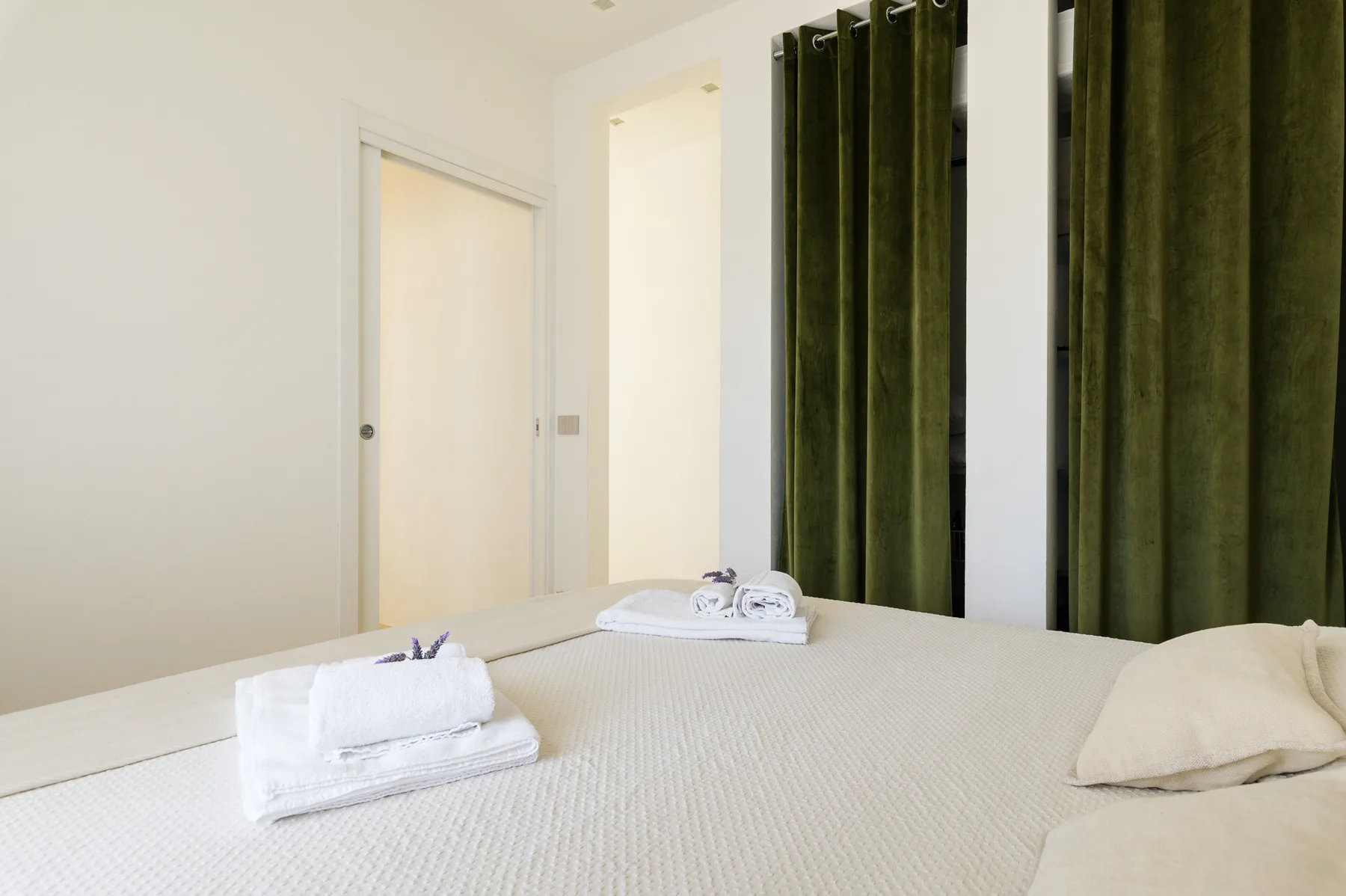 A bright bedroom with a neatly made bed and folded towels.