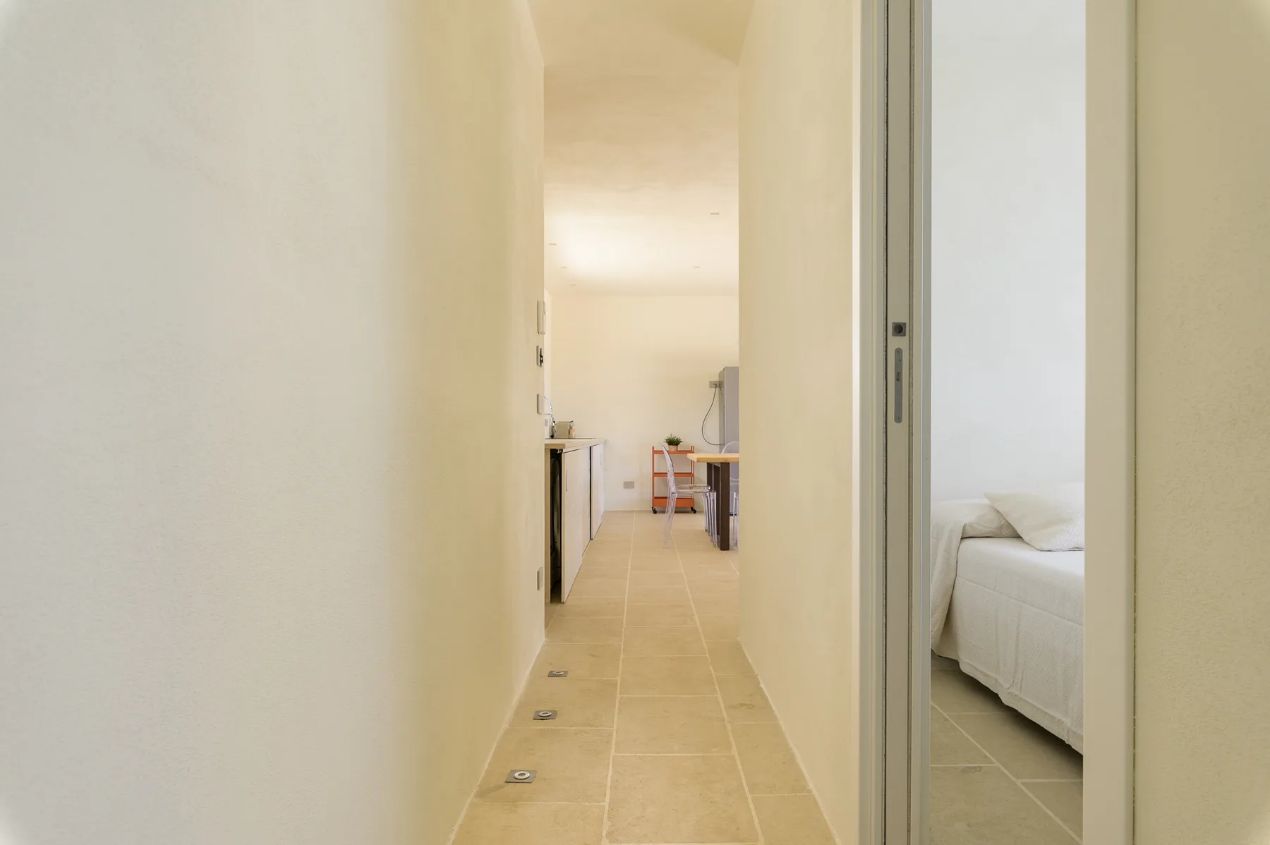 A narrow hallway leads to a small dining area, with a bedroom visible through a doorway.