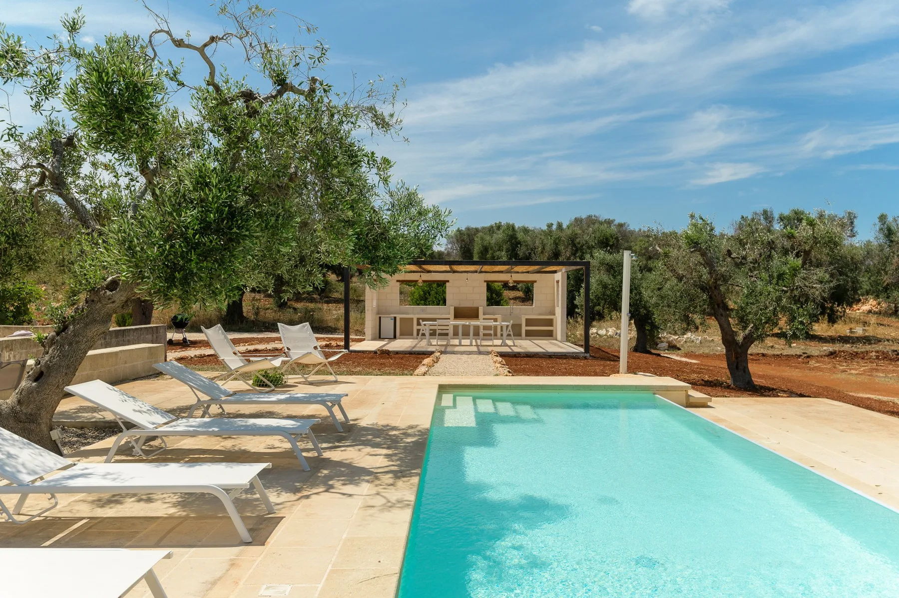 An outdoor pool beside a shaded seating area, surrounded by trees.
