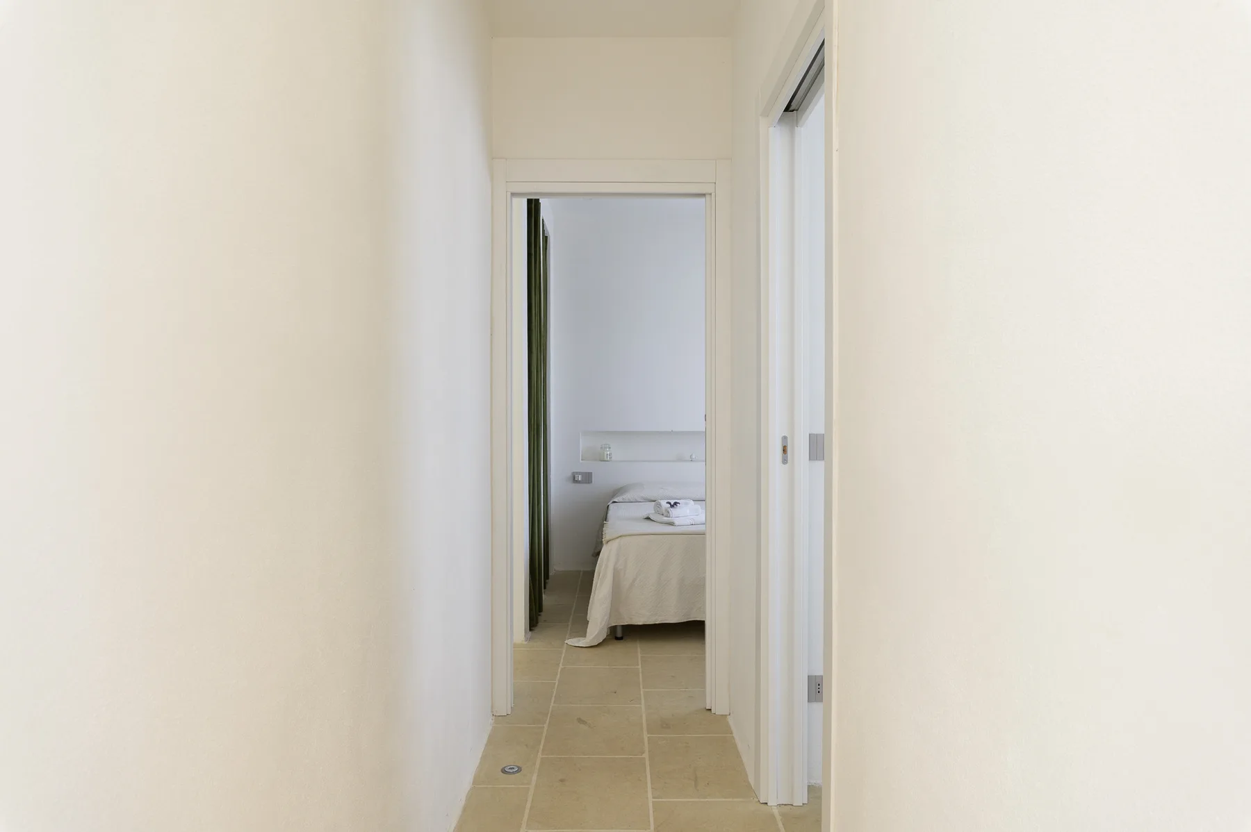 A hallway leads to a bedroom with a bed visible through the doorway.