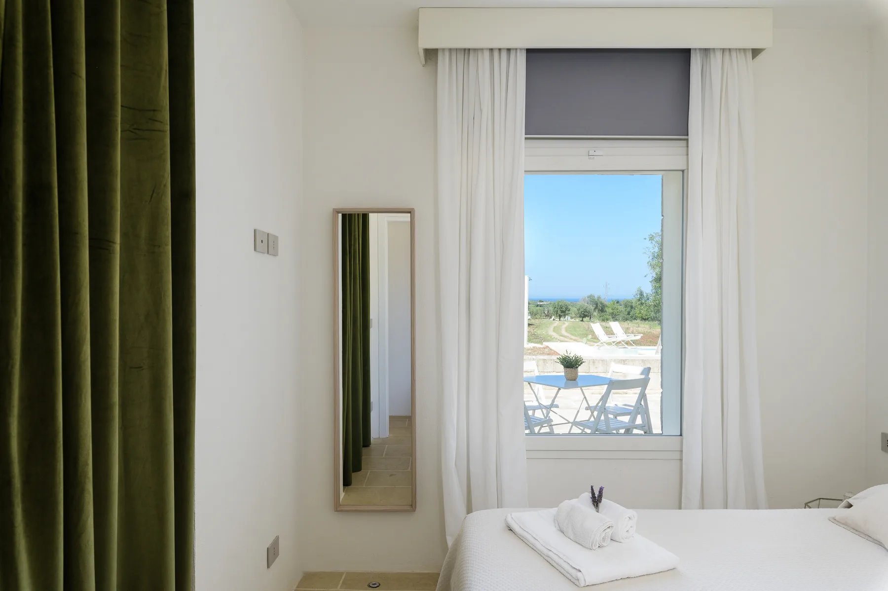 A bedroom with a bed beside a window overlooking an outdoor seating area.
