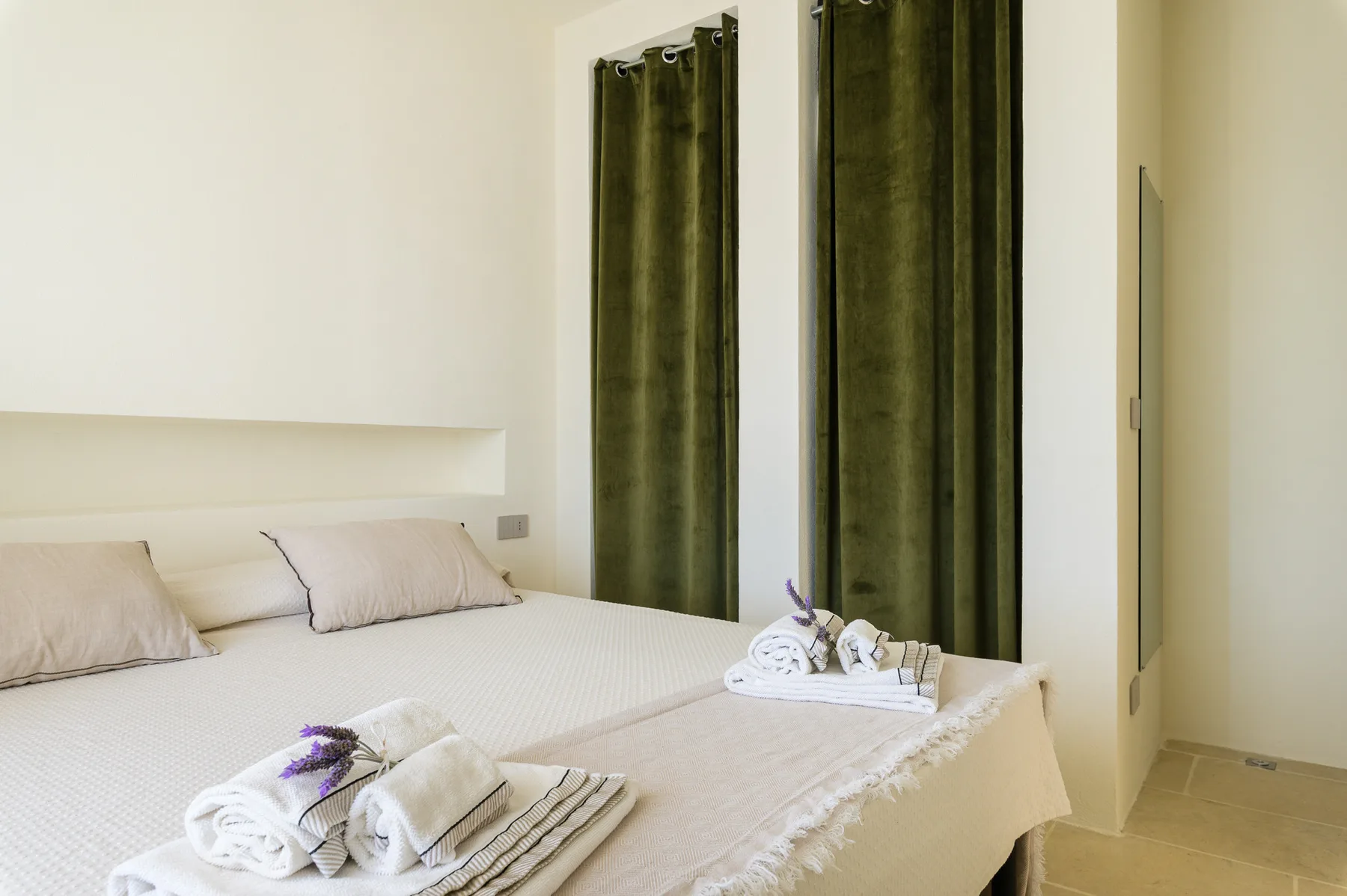 A bedroom with a neatly made bed and dark curtains.