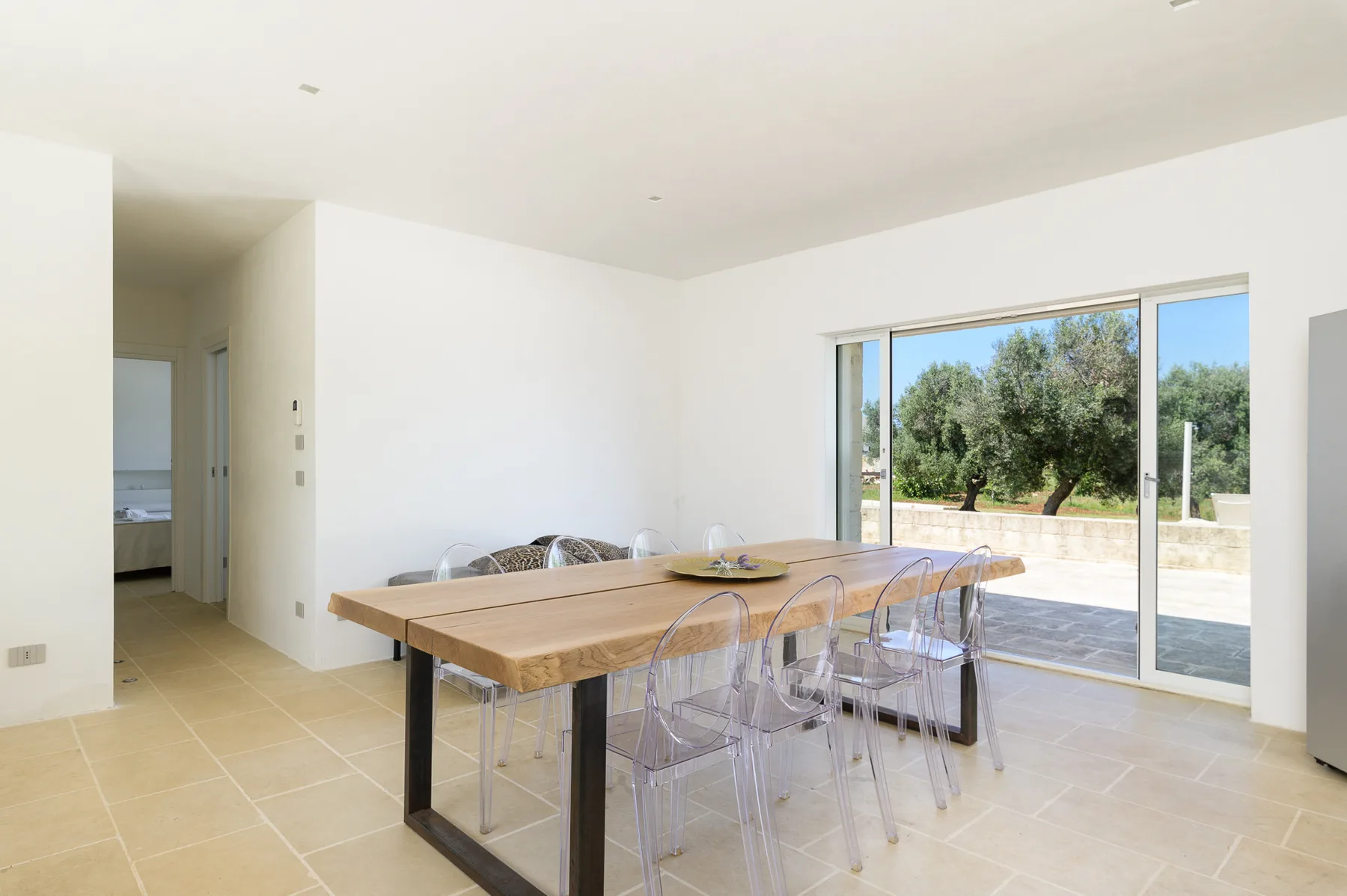 A bright dining area with a long table beside large sliding glass doors.