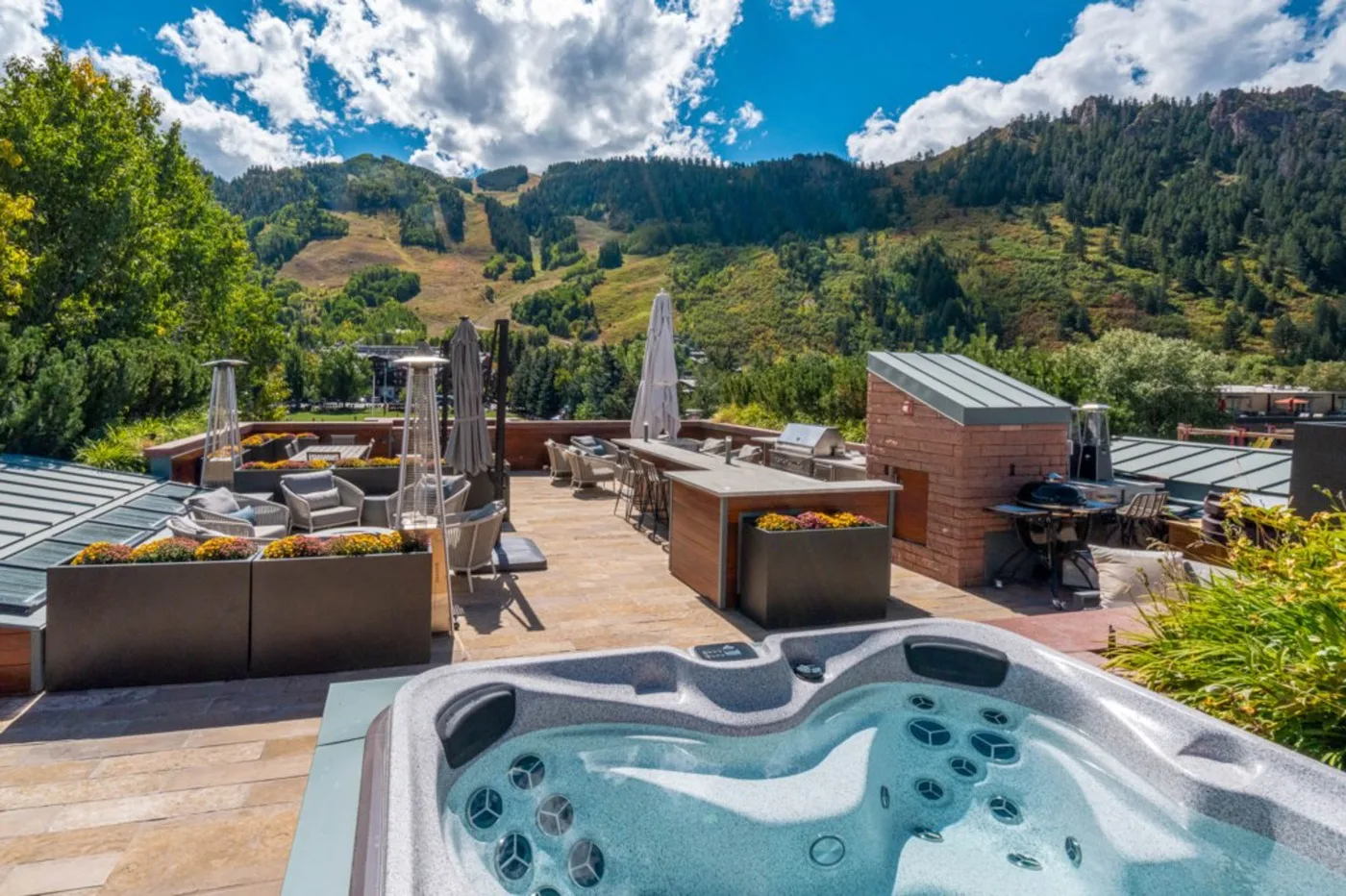 A rooftop terrace overlooks a wooded hillside, with a hot tub in the foreground.