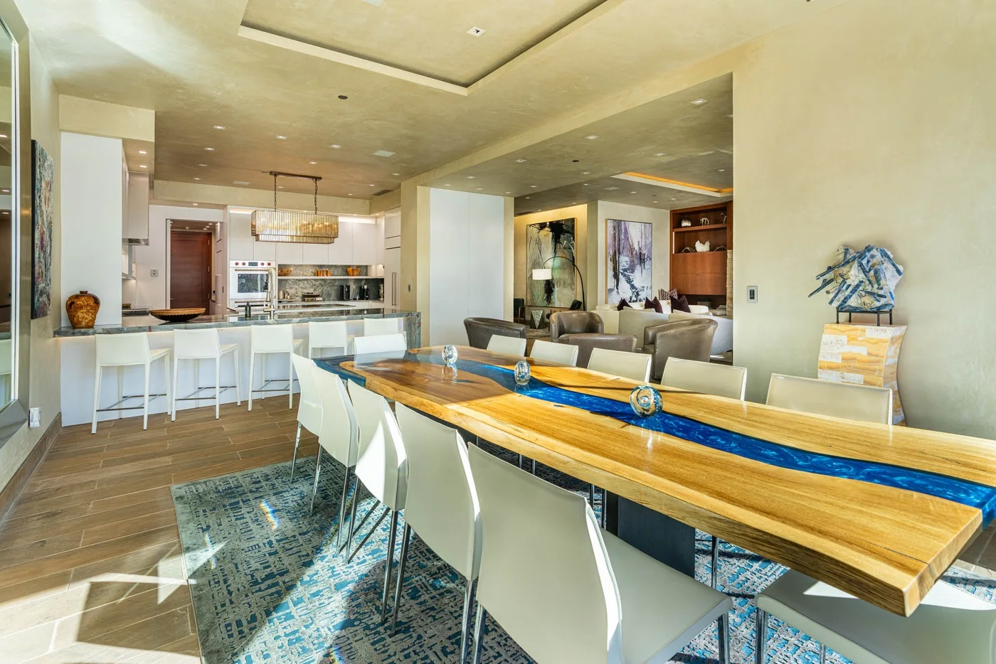 An open-plan dining area with a long table beside a kitchen and lounge seating.