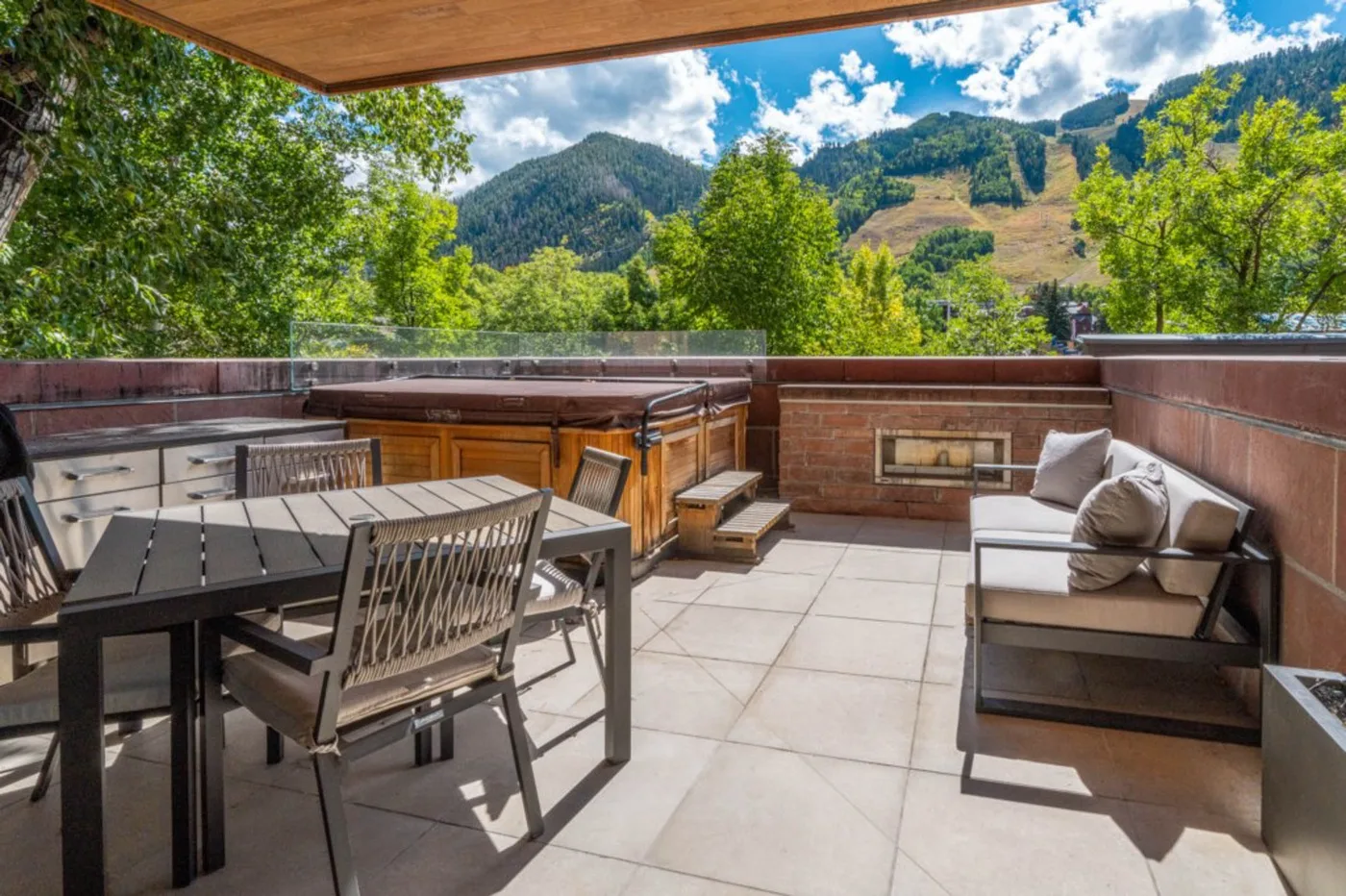 An outdoor terrace with dining seating and a lounge area overlooks green mountains.