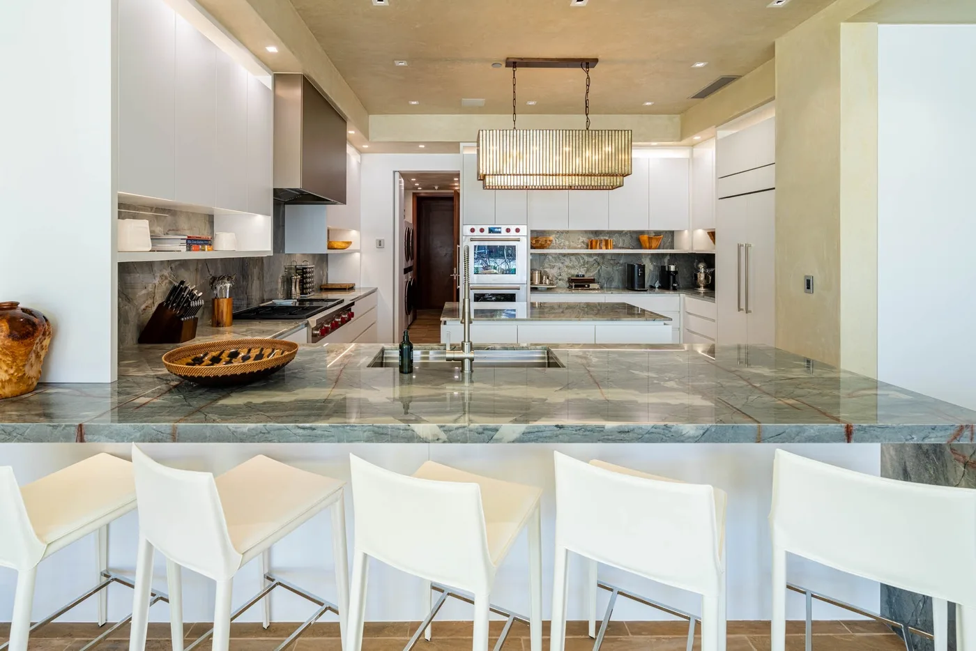 A modern kitchen with a long stone island and white seating.