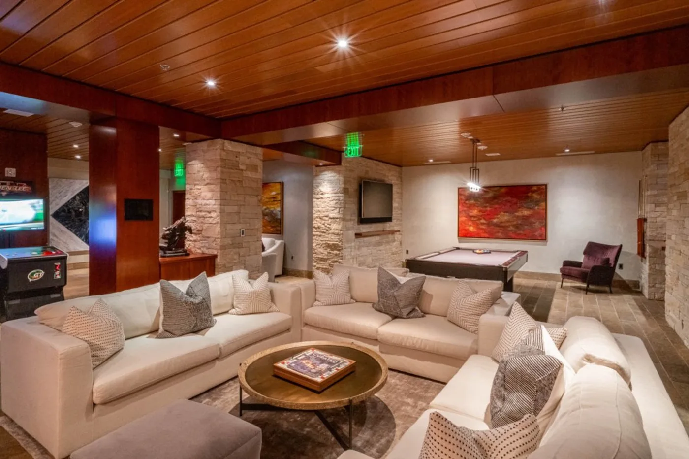 A lounge with seating arranged around a low coffee table beneath a wood-paneled ceiling.