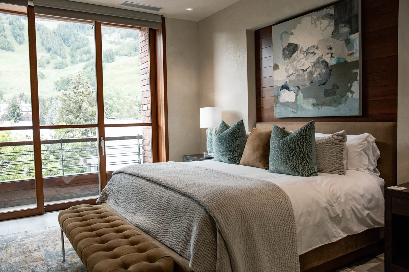 A bedroom with a neatly made bed and large windows overlooking a green landscape.