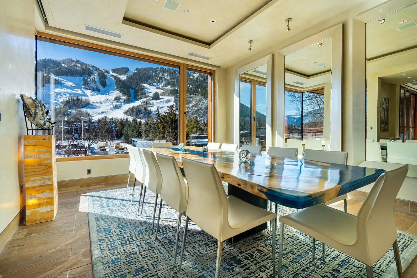 A dining area with a long table and large windows overlooking a snowy mountain landscape.