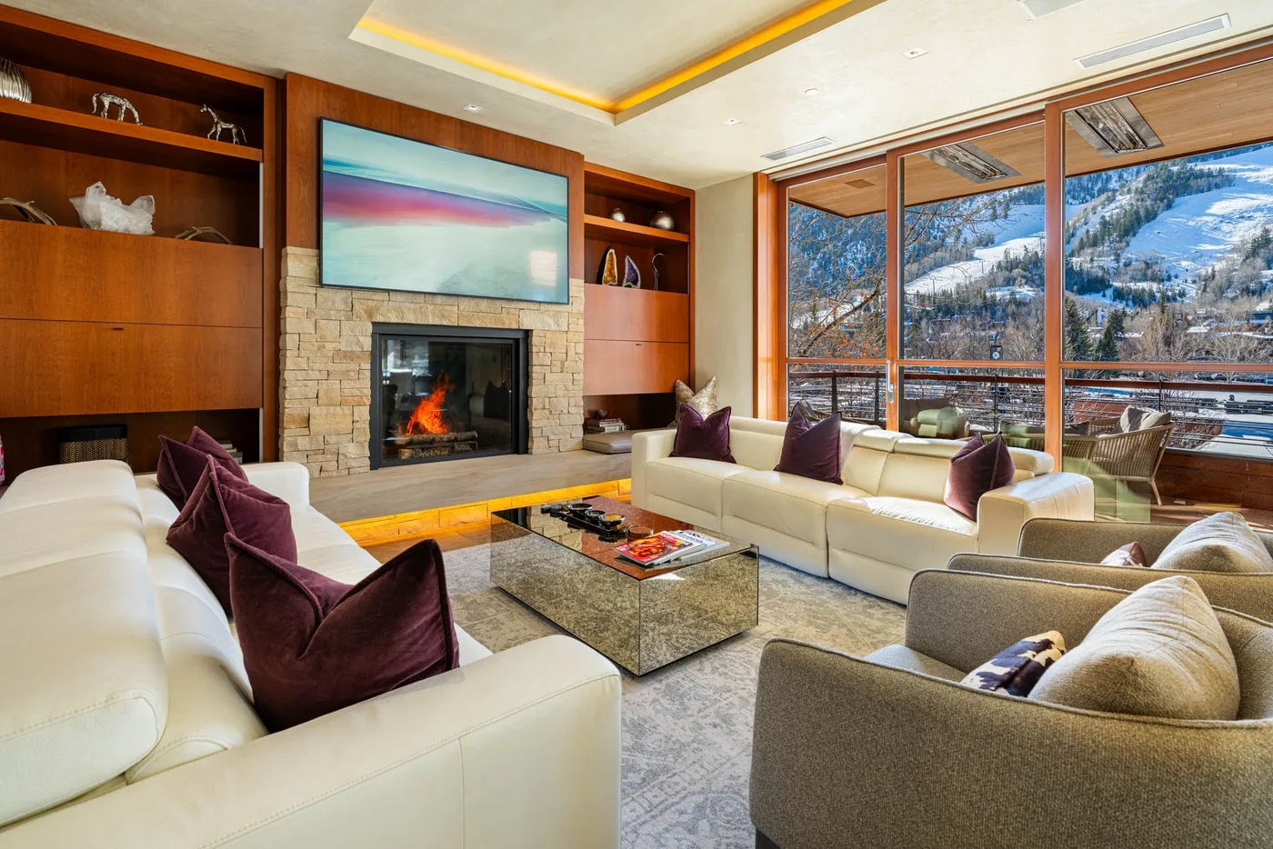 A spacious living room has seating arranged around a fireplace and large windows.