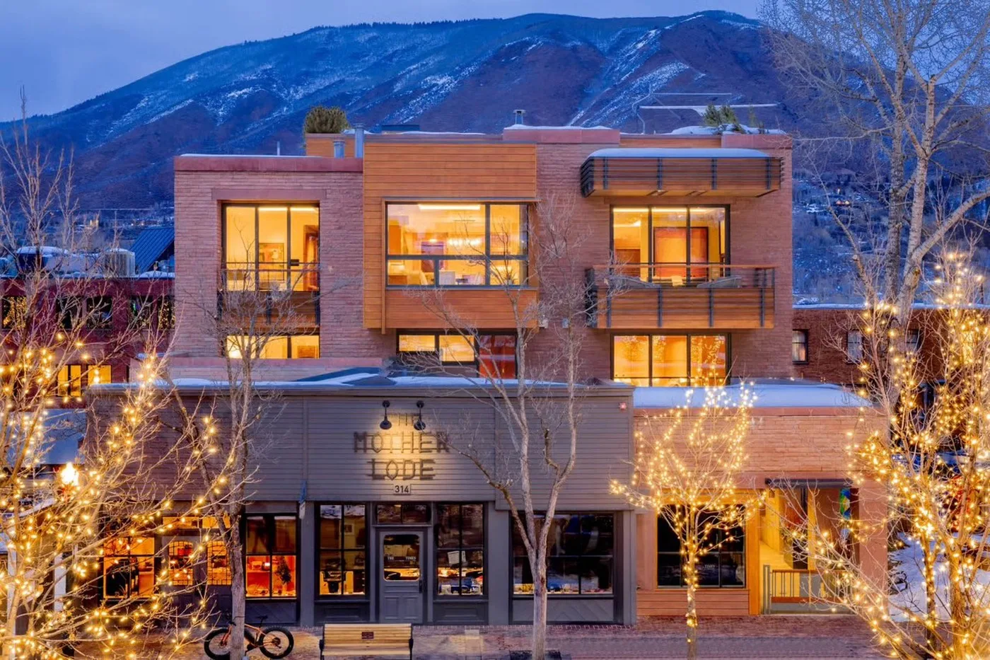 A modern lodge building glows with warm lights against a mountain backdrop.
