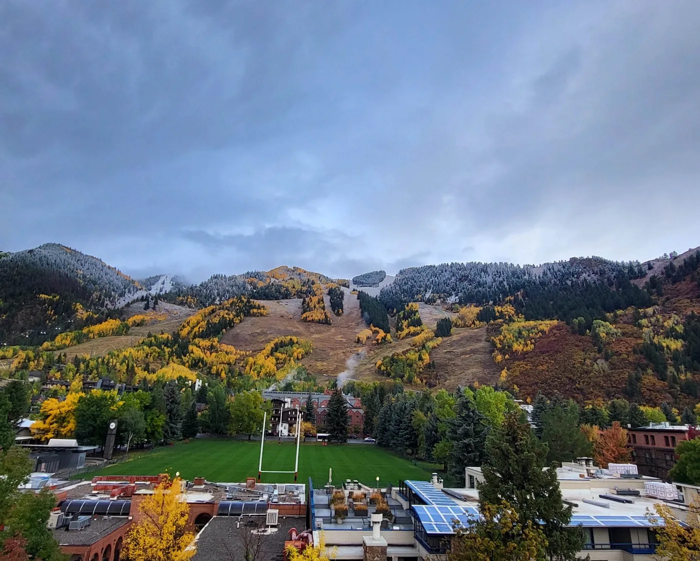 A mountain landscape with autumn-colored trees rises behind a green field.