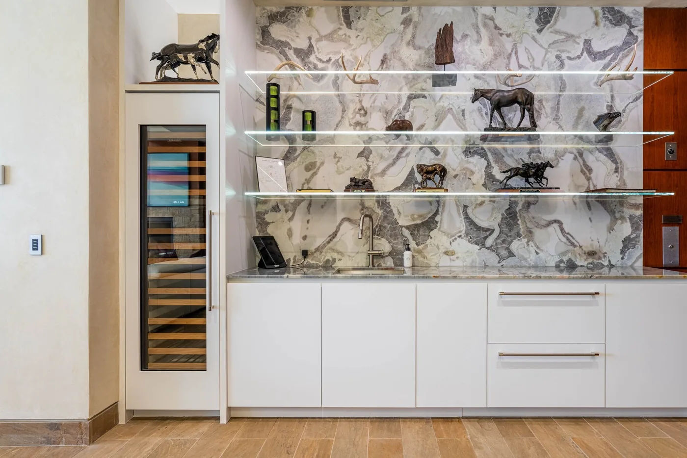 A modern kitchen with white cabinetry, a stone-patterned backsplash, and decorative objects on display.