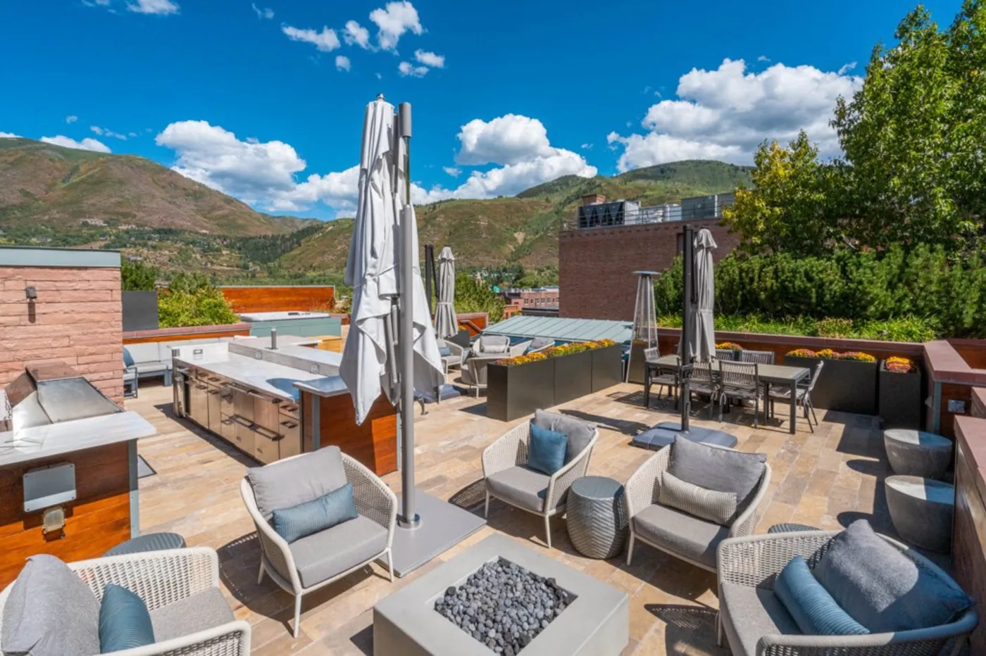 An outdoor terrace with seating, tables, and closed umbrellas overlooks a mountain landscape.