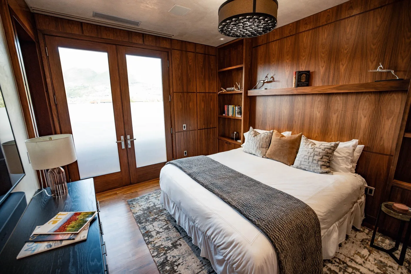 A bedroom with a bed, wood-paneled walls, and bright glass doors.