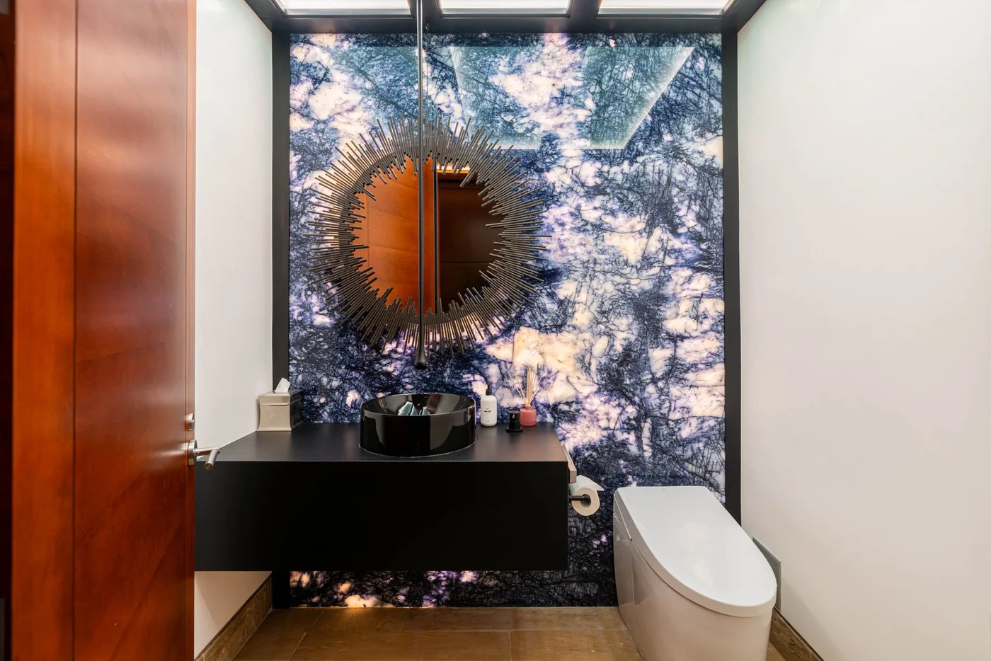 A bathroom with a dark vanity, vessel sink, and patterned wall behind the mirror.