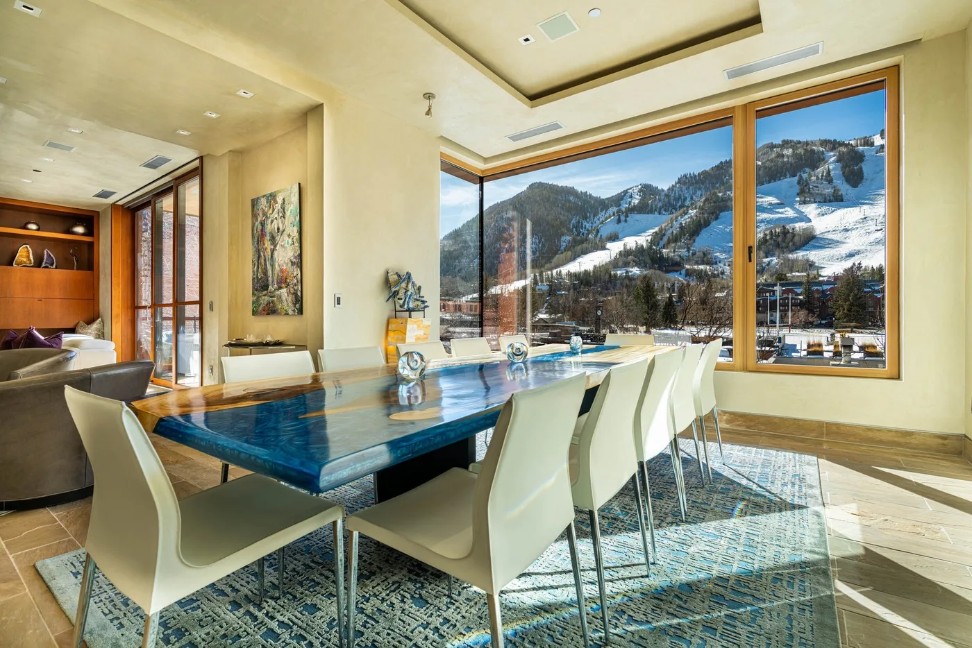 A dining area with a long table and large windows overlooking snowy mountains.