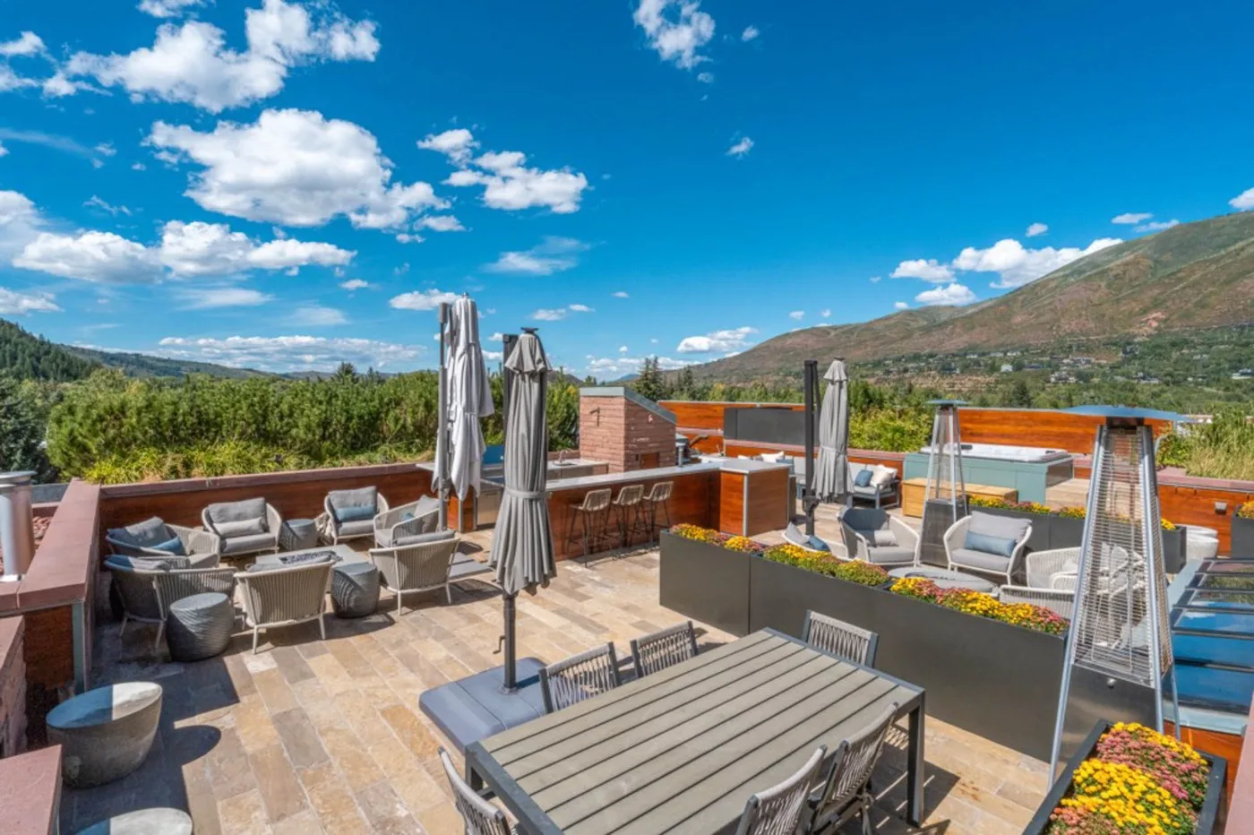 An outdoor terrace has seating, dining tables, and views of the surrounding hills.