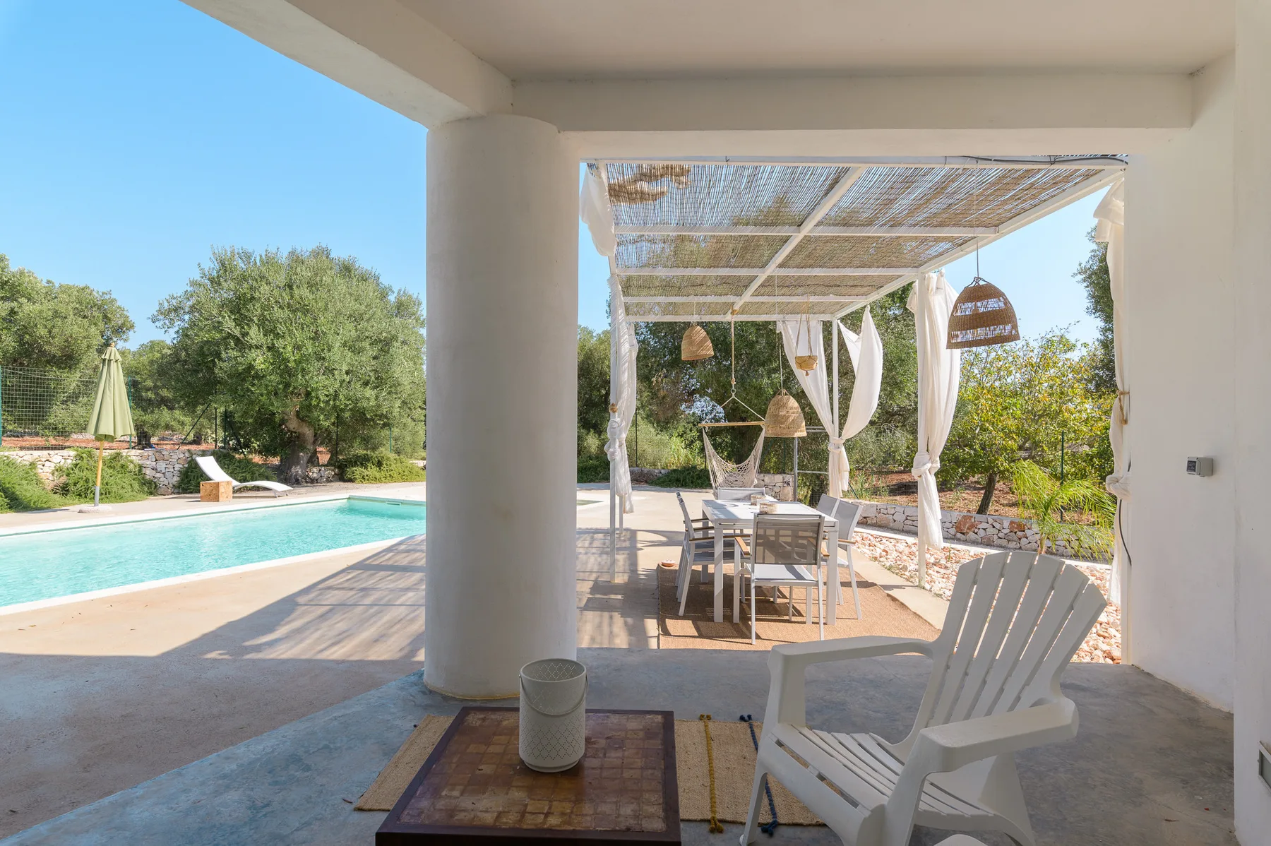 A covered outdoor dining area with white seating beside a swimming pool.