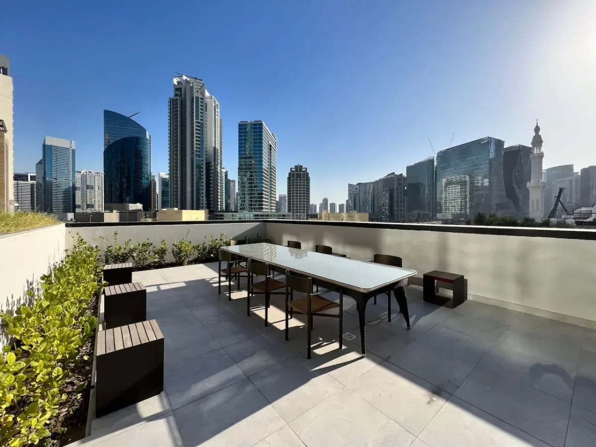 Una terraza en la azotea con asientos y una mesa al aire libre da a un horizonte urbano.