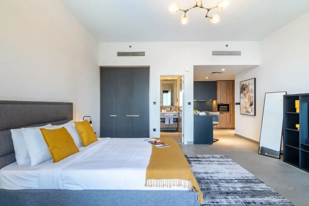 Un dormitorio con la cama arreglada y una vista abierta hacia la cocina.