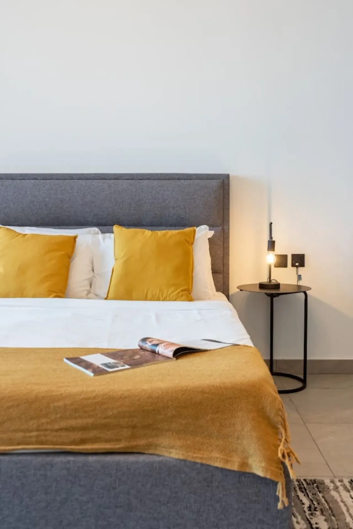Dormitorio con una cama vestida de blanco y ropa de cama mostaza.