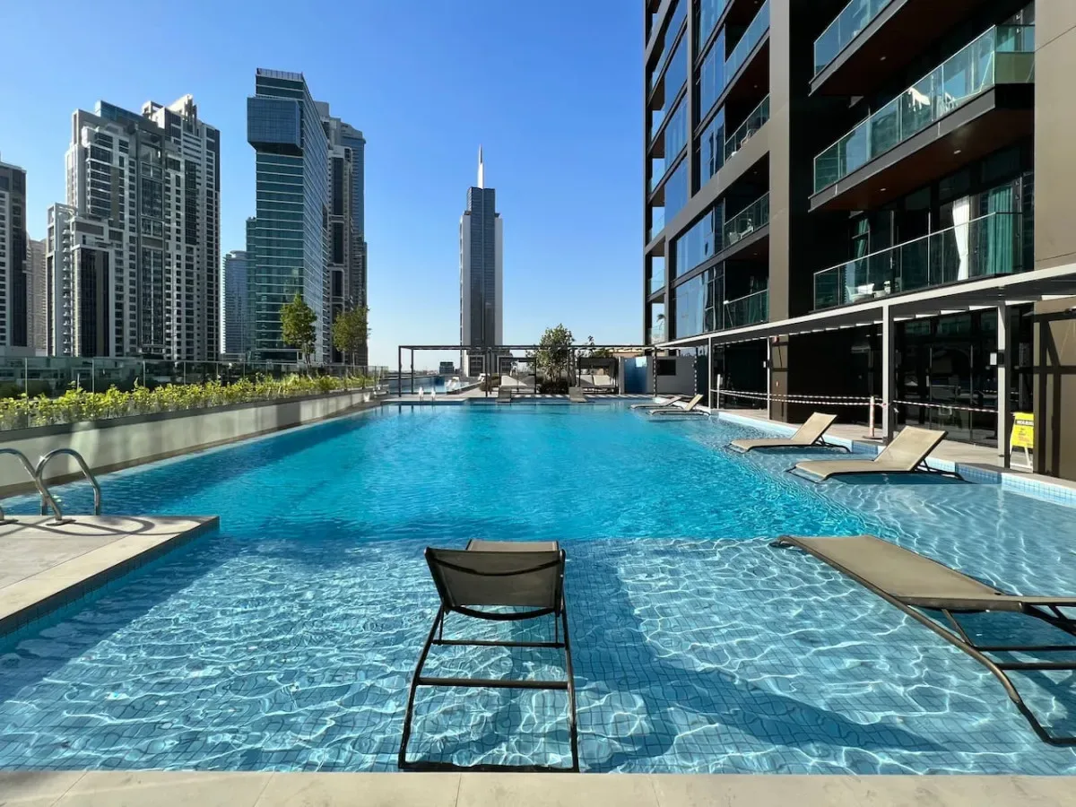 A rooftop swimming pool beside modern high-rise buildings under a clear blue sky.