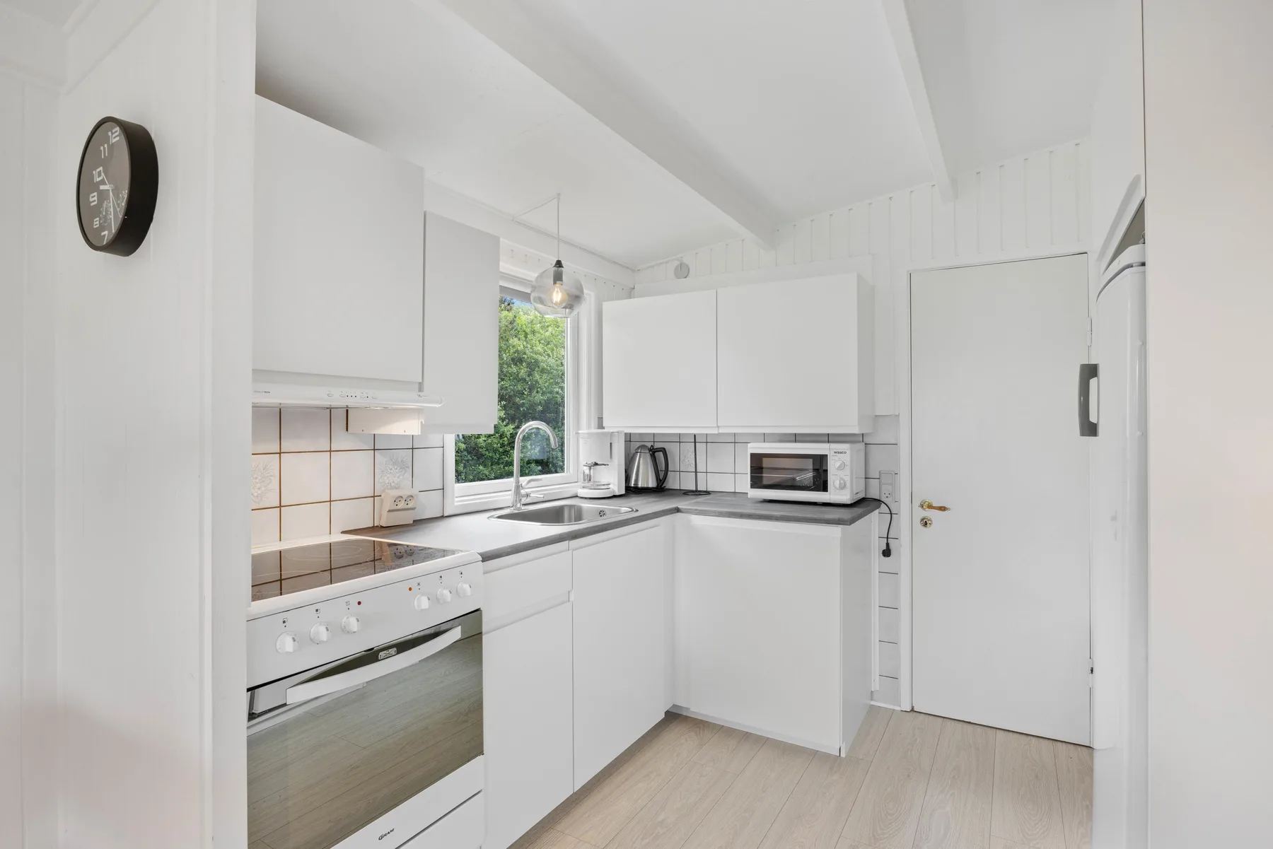 Una cocina blanca y luminosa con una encimera, un horno y una ventana.