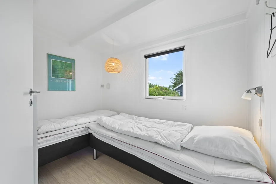 Un dormitorio luminoso con ropa de cama blanca y una ventana con vistas a la vegetación.