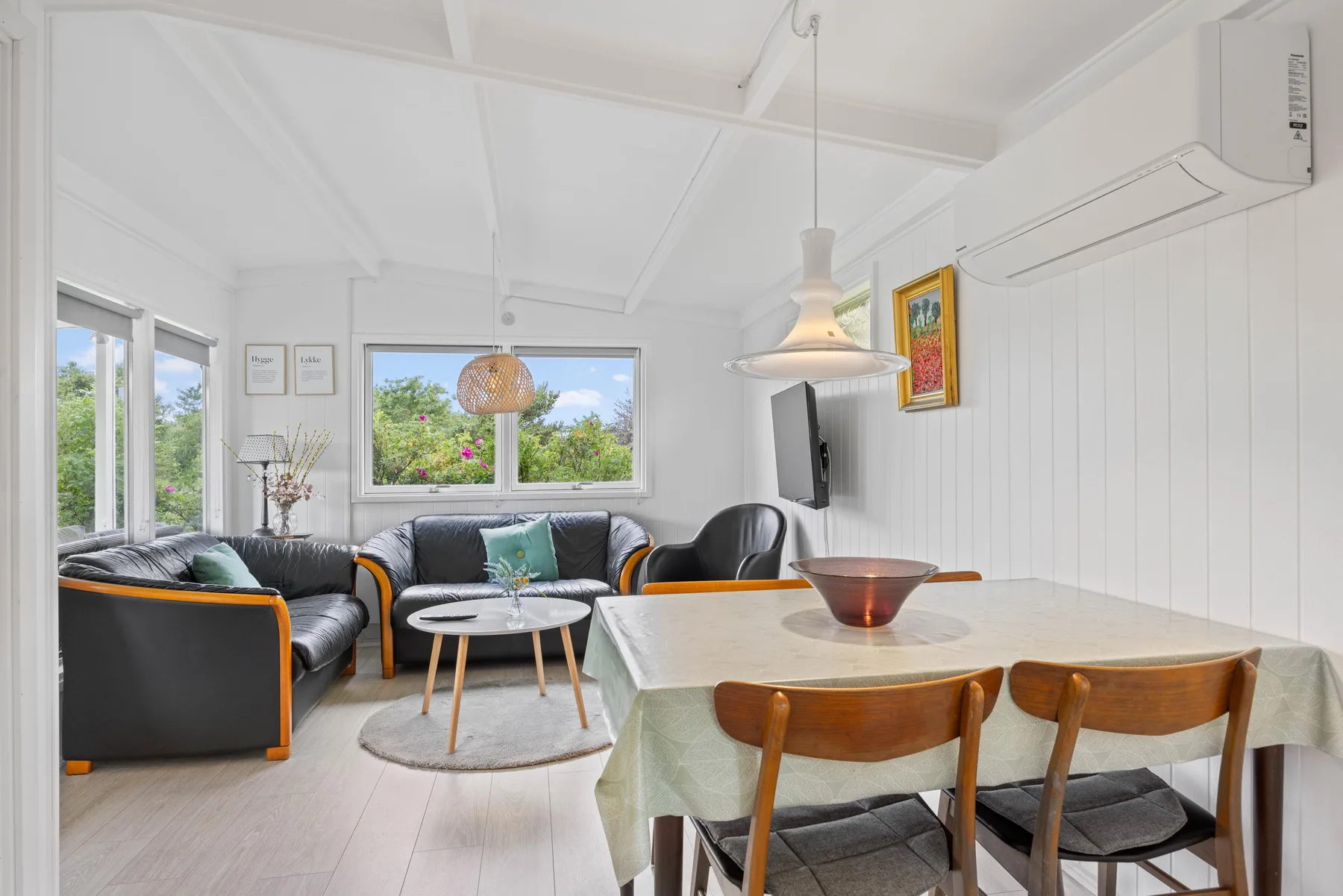 Una luminosa sala de estar y comedor con asientos alrededor de una mesa y amplias ventanas.