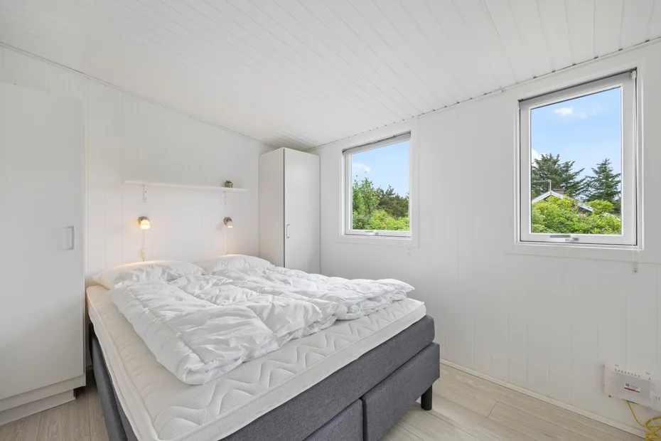 Un dormitorio luminoso con una cama grande y dos ventanas.