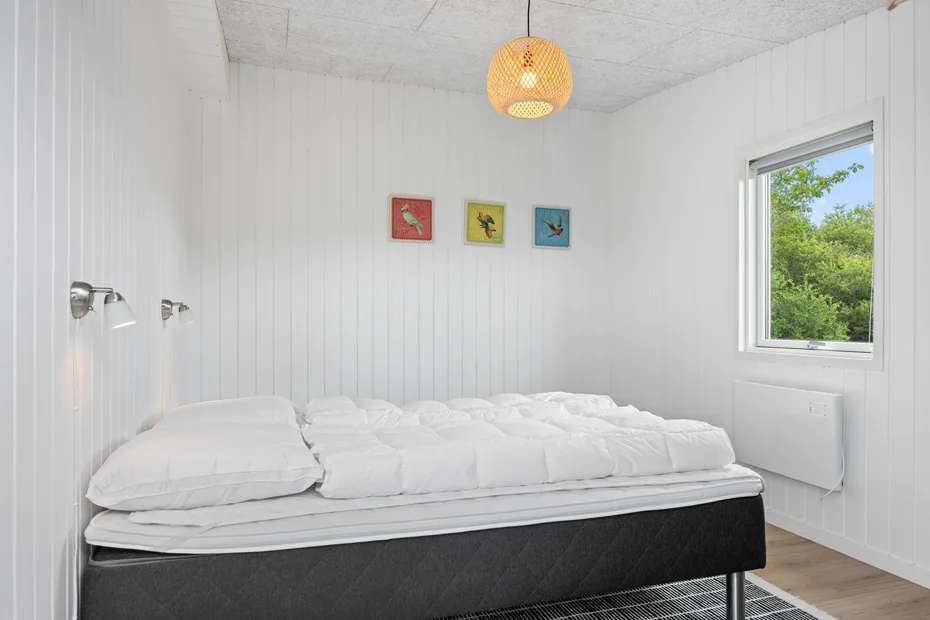 Un dormitorio con una cama bajo tres pequeños cuadros coloridos.