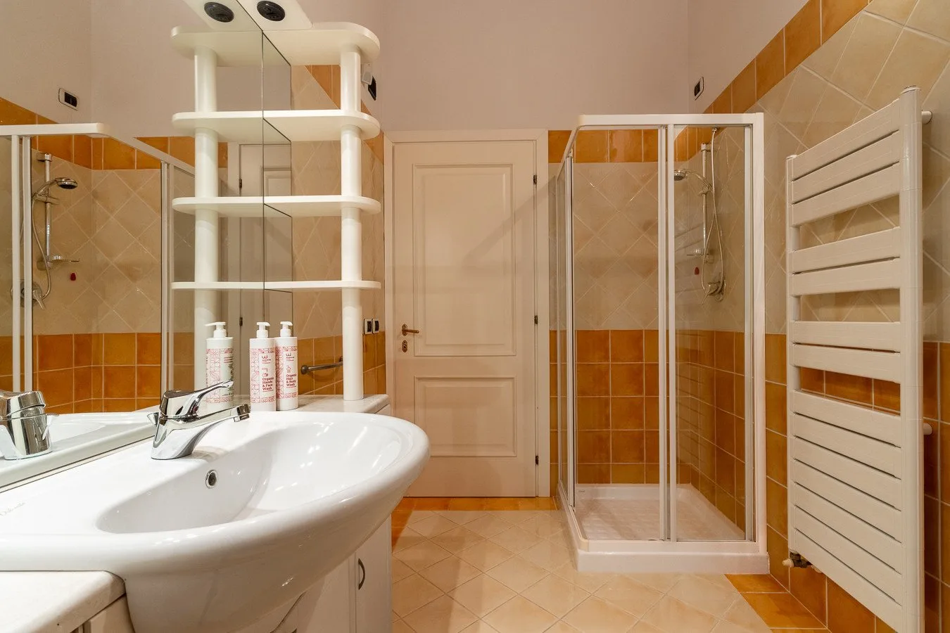 A tiled bathroom with a sink, shower, and towel radiator.