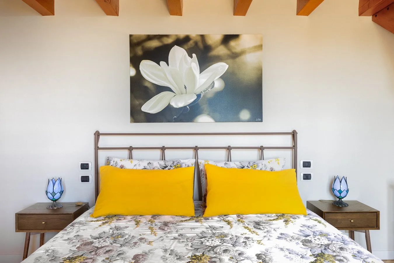 A bedroom with a double bed, yellow pillows, and floral bedding.