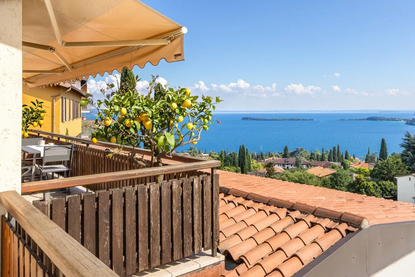 A terrace overlooks rooftops, greenery, and a broad blue expanse of water.