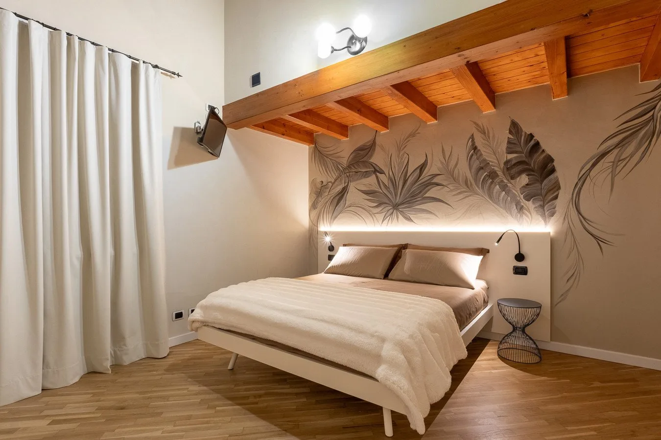 A bedroom with a bed beneath exposed wooden ceiling beams and a botanical wall mural.