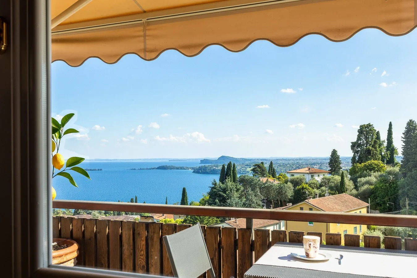A balcony dining area overlooks a blue lake beneath a retractable awning.