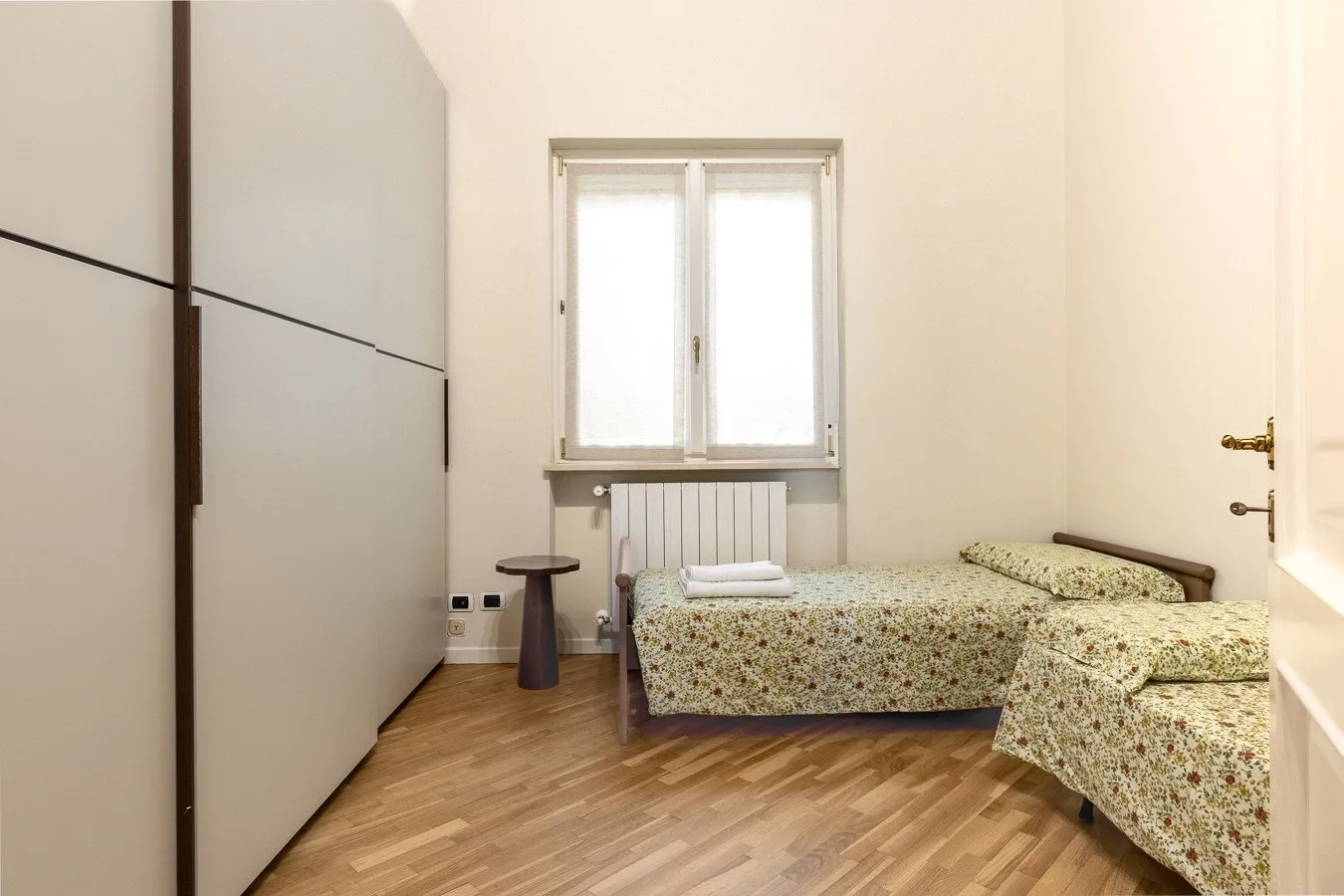 A bedroom with two beds, a window, and a wardrobe.